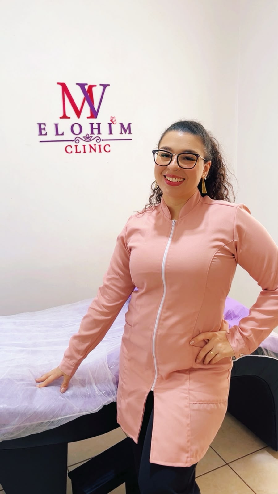 Milena Vigatto na sala de atendimento da Elohim Clinic, ao lado da maca e da marca aplicada na parede